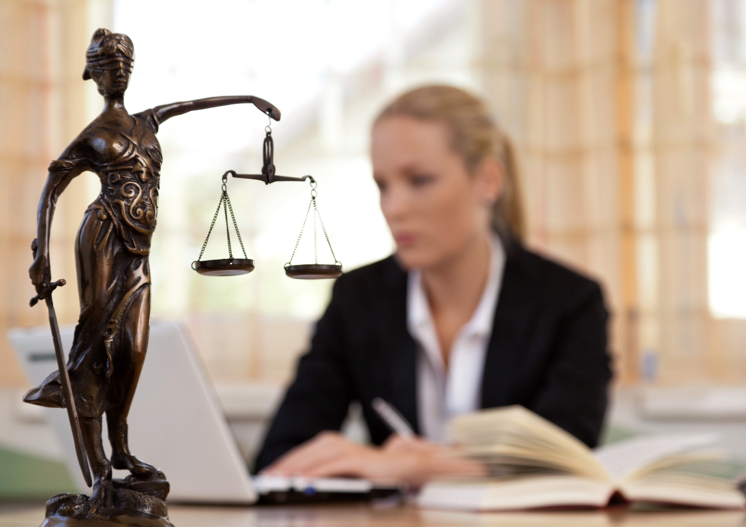 When To Raise An Estate Dispute | Gaslowitz Frankel | A woman sitting at her desk in her office in the background with a justiciary statue in the foreground